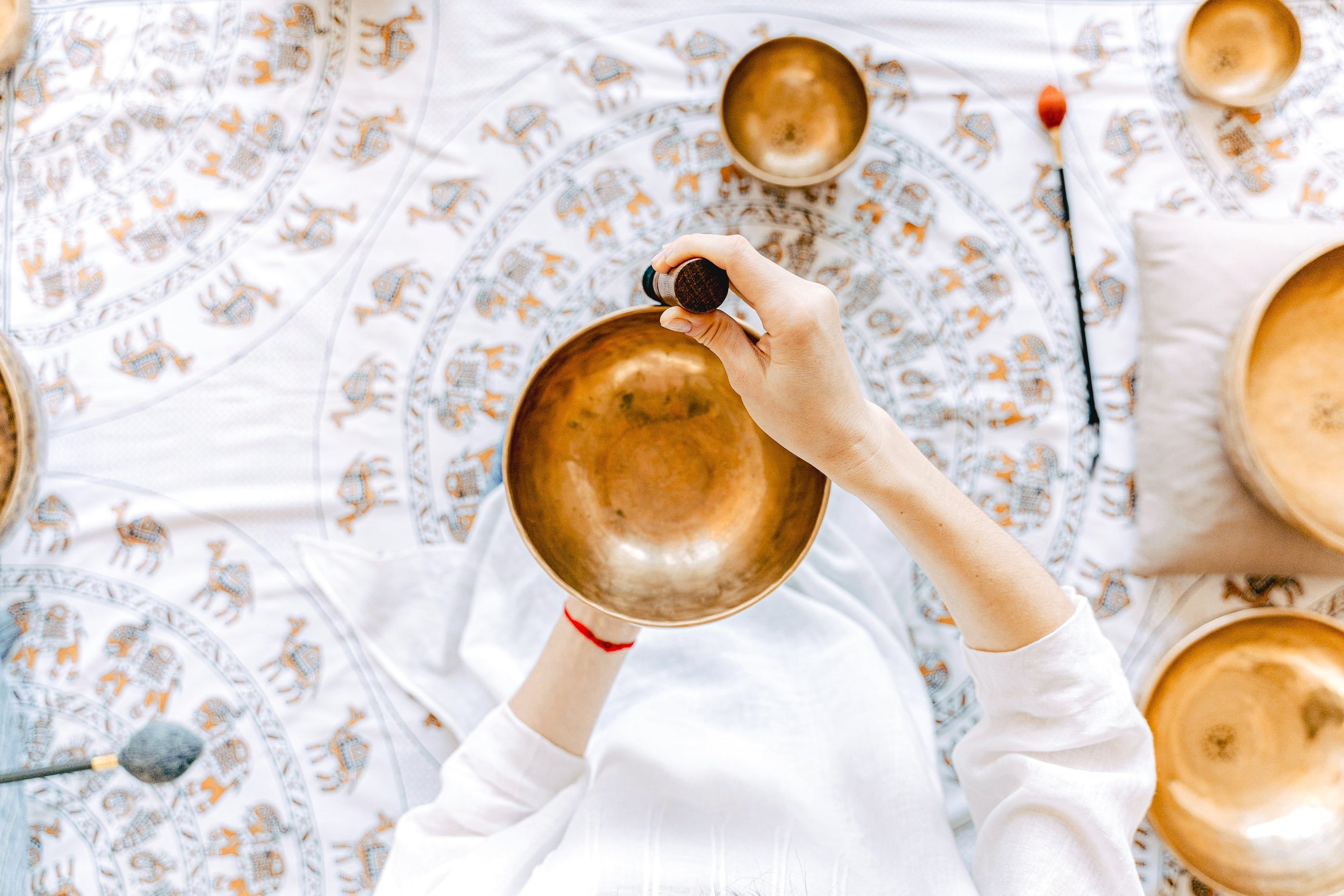Person playing a Tibetan singing bowl surrounded by multiple singing bowls, demonstrating proper technique and resonance