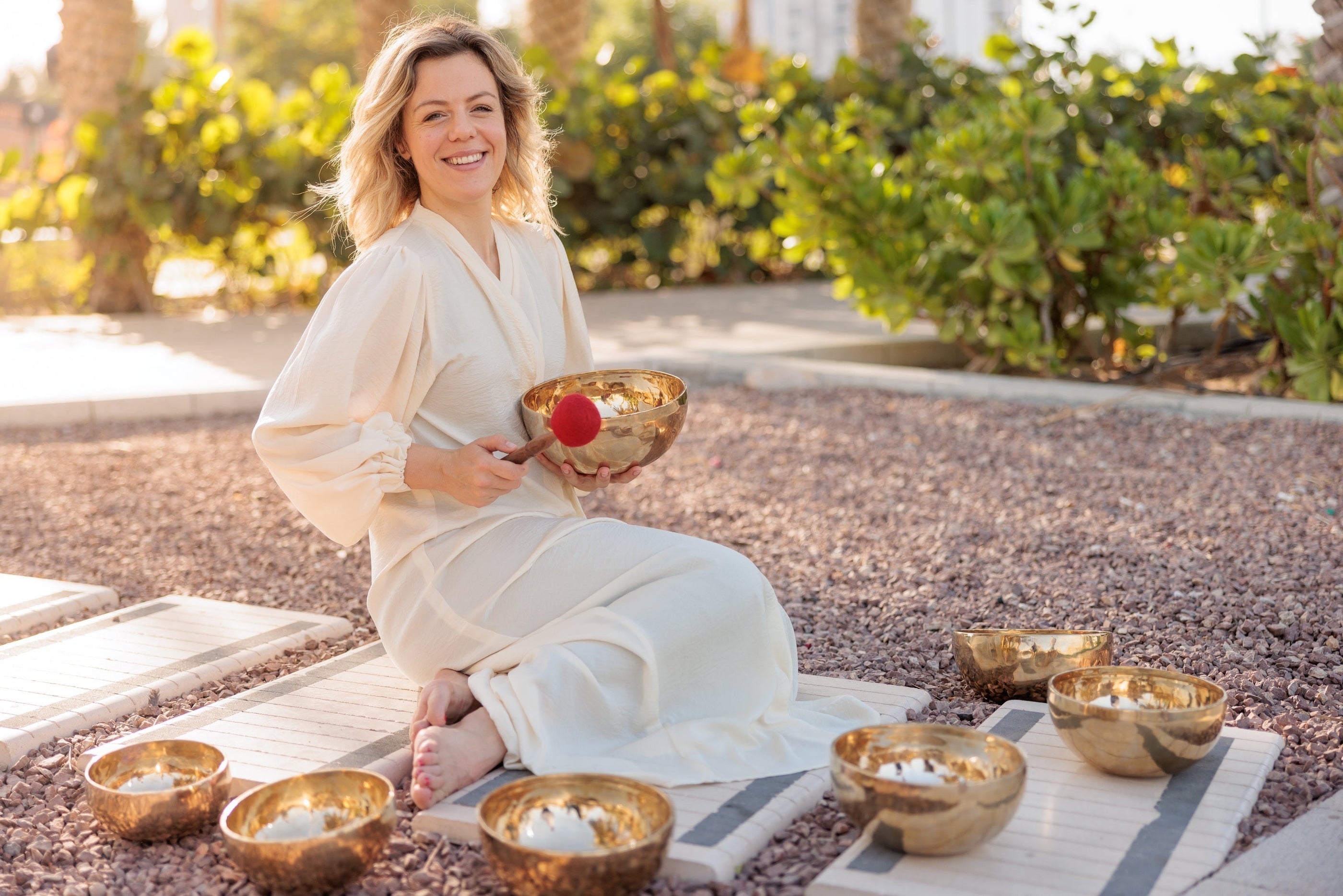 Woman smiling joyfully outdoors surrounded by Tibetan singing bowls, embodying the bliss and beauty of conscious living